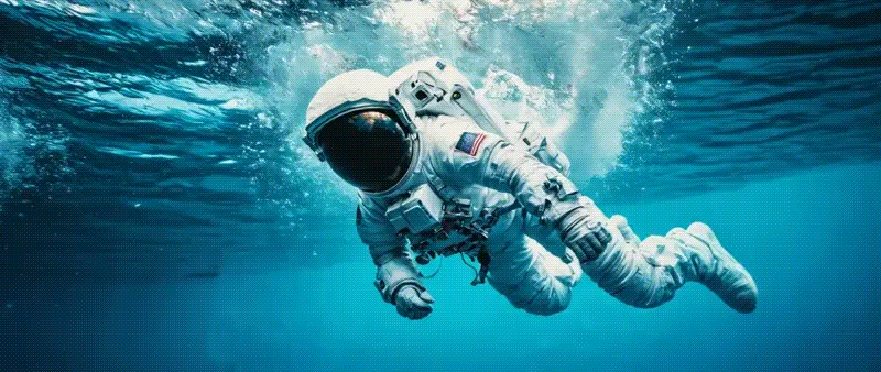 Astronaut in full white spacesuit floats underwater in a deep blue pool.